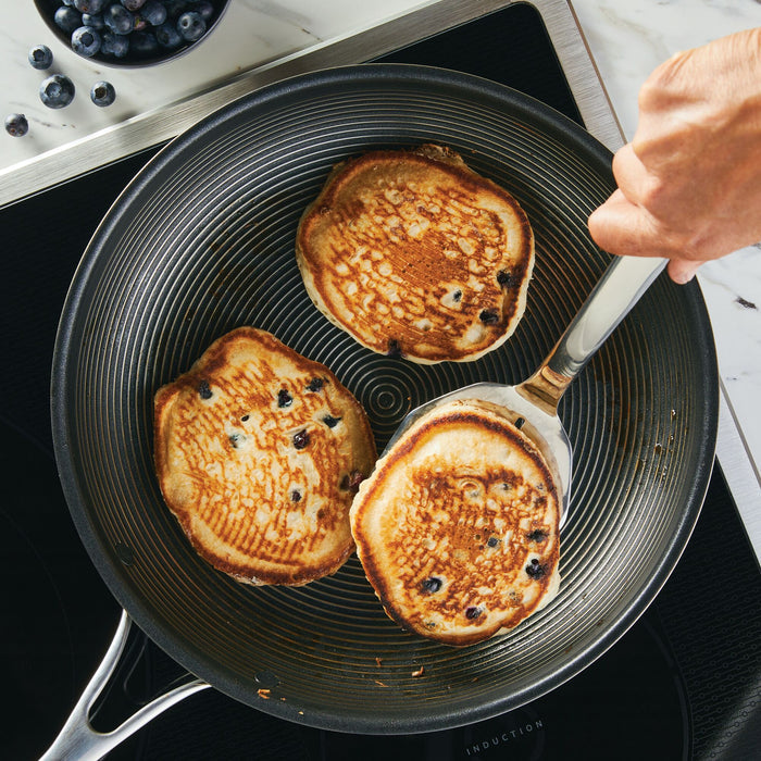 Three blueberry pancakes sizzle in a frying pan on the stove, surrounded by the 3-Piece Kitchen Utensils Set with ergonomic handles, ready for effortless flipping.