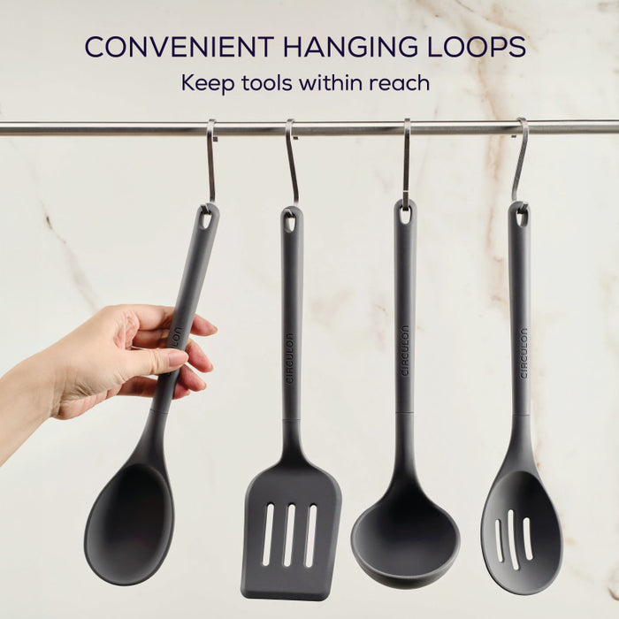 A hand holds one from the 4-Piece Silicone Tools Set, as three hang on hooks.