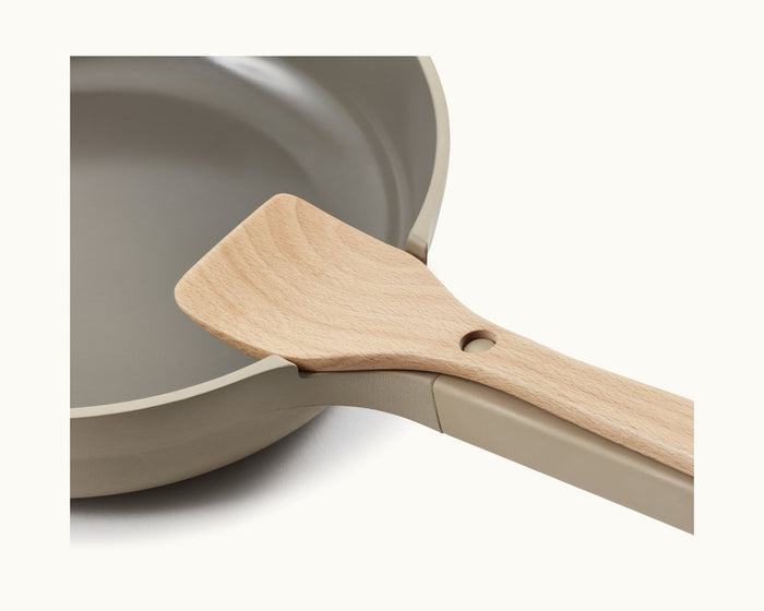 A close-up of a beige frying pan with a Beechwood Spatula resting on its edge, highlighting premium kitchen accessories.