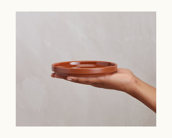 A hand holds a round, shallow Dessert Plate with a scratch-resistant ceramic finish against a light neutral background, highlighting its quality as part of an elegant tableware set.