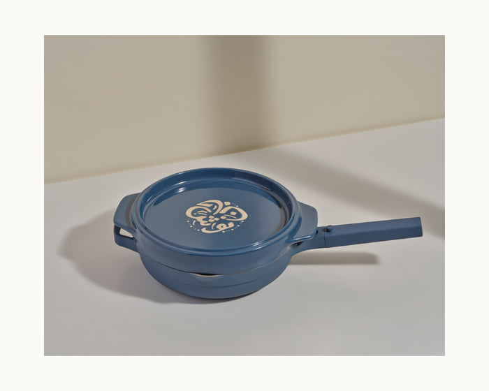 The Flipping Platter, a blue ceramic saucepan with lid and white decorative pattern, sits on a white surface—ideal for preparing tahdig or serving maqluba straight from the stovetop.
