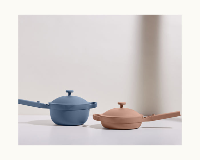 The Mini Cookware Duo—featuring a matte-finish blue Mini Perfect Pot and beige Mini Always Pan—rests side by side on a white surface with a neutral background.