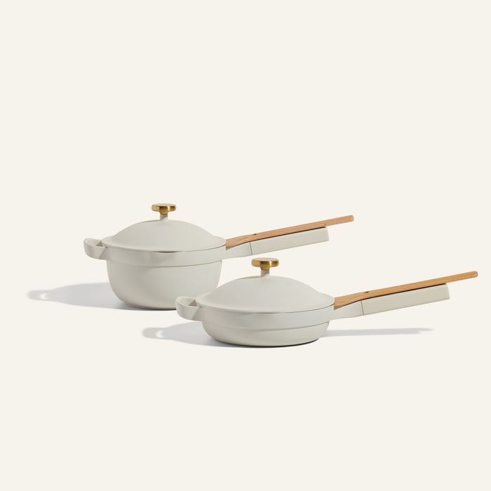 The Mini Cookware Duo features two white ceramic pots with wooden handles and gold lids, displayed side by side on a light background to highlight their multifunctional design.