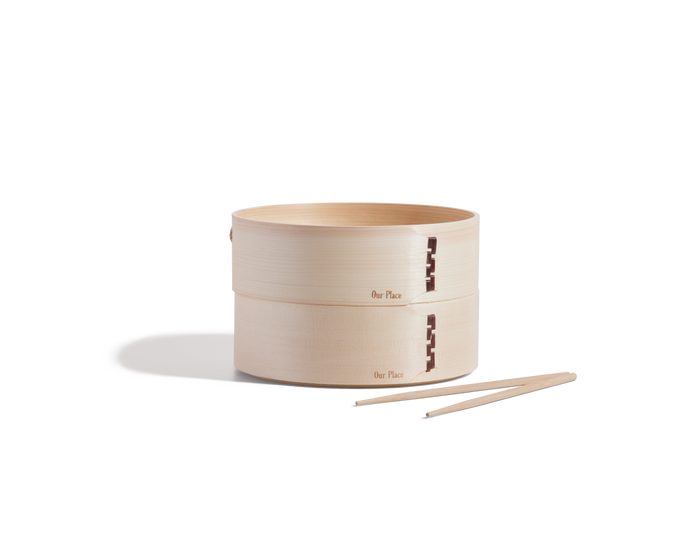 Two Mini Spruce Steamers, handcrafted by Chinese artisans and engraved with "Our Place," are stacked together next to a pair of bamboo chopsticks on a white background.