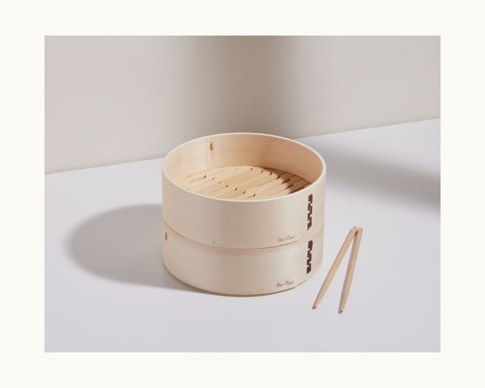 A handmade Mini Spruce Steamer with two tiers sits on a white surface beside bamboo chopsticks, crafted by Chinese artisans.