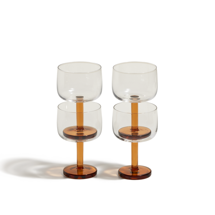 Four Party Coupes with clear glass bowls and amber-colored stems and bases are arranged in two rows on a plain white background, perfect for serving vibrant party drinks.