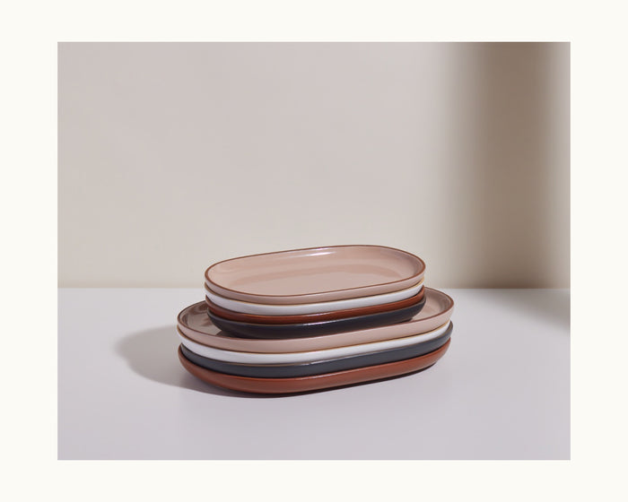 A stack of six Serving Platters in beige, brown, and white ceramic ovals rests on a white surface against a neutral background, making a stylish tableware set.
