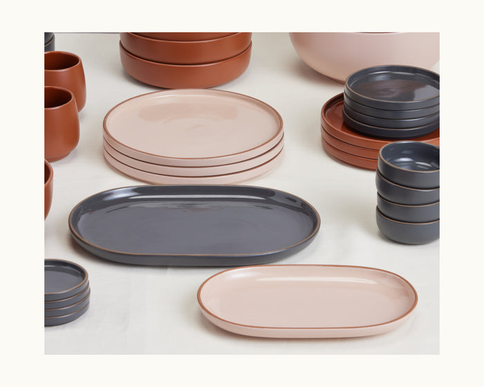 Serving Platters: A set of ceramic dishware in soft tones—plates, bowls, cups, and curved platters—arranged neatly on a light surface.