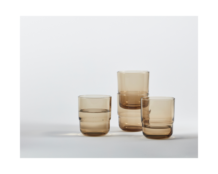 Four Short Night + Day Glasses made of translucent brown recycled glass are displayed on a white surface, with two glasses stacked atop each other.