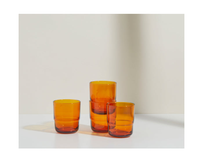 Four Short Night + Day Glasses, made of amber-colored recycled glass, are arranged on a white surface against a light background.