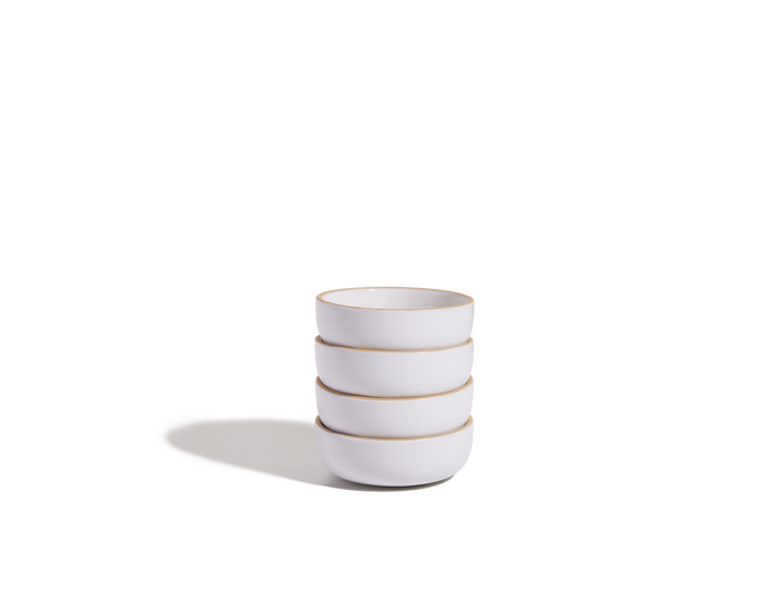 A stack of four Tiny Bowls, made from scratch-resistant ceramic with light brown rims, sits on a white surface with a shadow on the left.