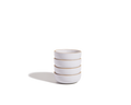 A stack of four Tiny Bowls, made from scratch-resistant ceramic with light brown rims, sits on a white surface with a shadow on the left.