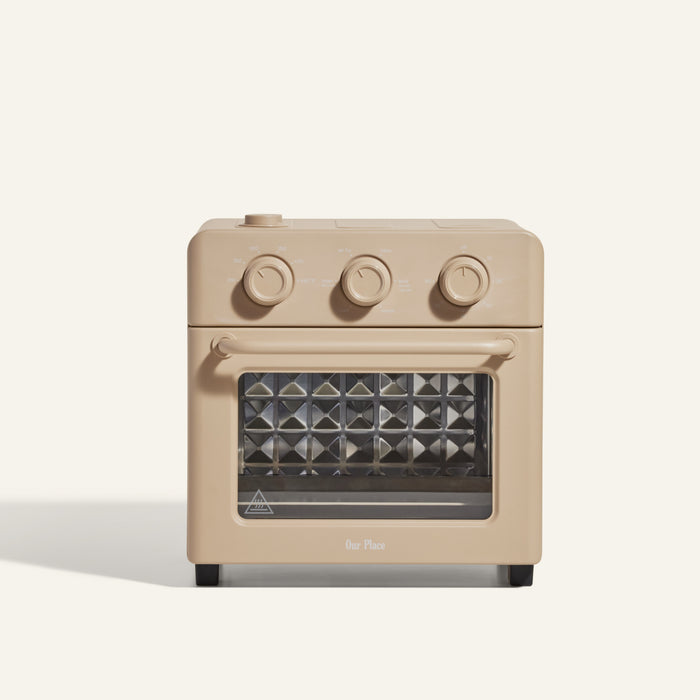 The Wonder Oven is a beige countertop oven with air fryer functionality, featuring three control knobs and a glass door, shown against a plain light background.